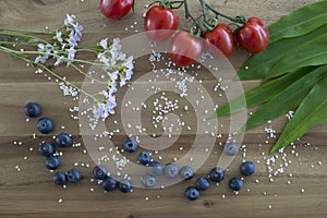 Blueberries, fresh wildflowers, red tomatoes, fresh green bear onions. Perfect background with healthy fit food on wooden cutting