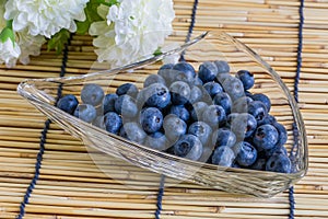 Blueberries in the glass bowl on the wooden background with white flower
