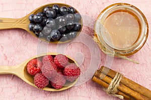 Blueberries and raspberries in a wooden spoon and a jar of honey with cinnamon on a pink napkin. Healthy vegetarian food