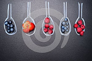 Blueberries, strawberries, raspberries, and a variety of berries, in painted chalk spoons, place text, top view