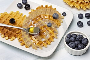 Blueberries in a white bowl. Spoon of honey, waffles and berries on a plate