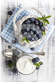 Blueberry basket and glass of yogurt on white wooden table