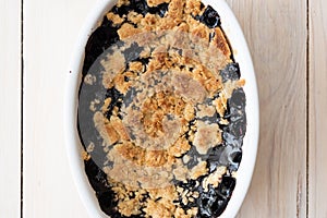 Blueberry crumble at white ceramic cooking pan on white pained wood background