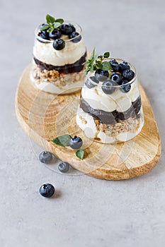 Blueberry dessert with curd cream and granola topping basil leaves in a glass cup.