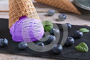 Blueberry ice cream in a waffle cup on a stone surface