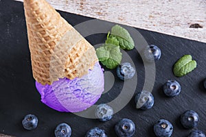 Blueberry ice cream in a waffle cup on a stone surface