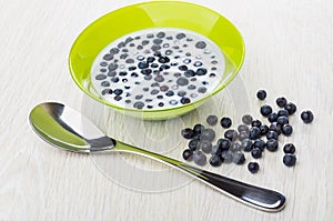 Blueberry with milk in bowl, scattered berries, spoon on table