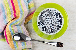 Blueberry with milk in bowl, spoon, striped napkin on table