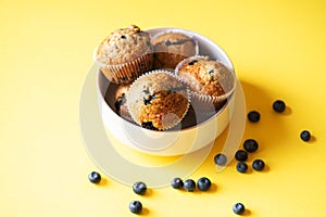 Blueberry muffins served in a bowl on a yellow background. Overhead view