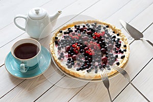 Blueberry open pie on blue plate on bright painted wood with cup of black tea