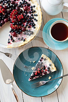 Blueberry open pie on blue plate with metal spatula close up with cup of black tea and tea pot