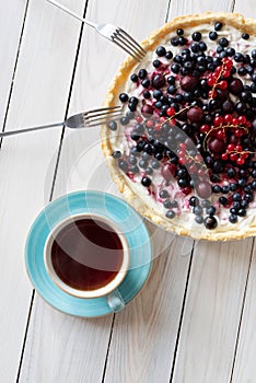 Blueberry open pie with cup of black tea on bright painted wood background