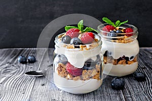 Blueberry, raspberry parfaits in mason jars, scene on dark background