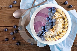 Blueberry smoothie bowl with coconut, bananas, chia seeds and granola, above scene on wood