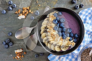 Blueberry smoothie bowl with coconut, bananas, chia seeds and granola, above view on a dark background