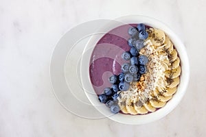 Blueberry smoothie bowl with coconut, bananas, chia seeds and granola, above view on a marble