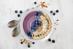 Blueberry smoothie bowl with coconut, bananas, chia seeds and granola, flat lay on marble