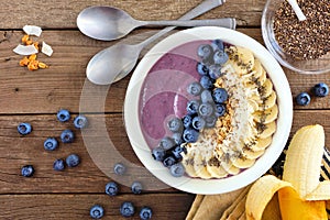 Blueberry smoothie bowl with coconut, bananas, chia seeds and granola, flat lay on wood