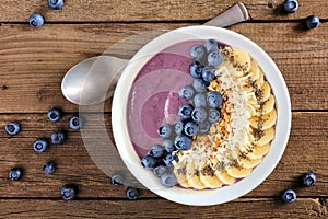 Blueberry smoothie bowl with coconut, bananas, chia seeds and granola, top view on wood