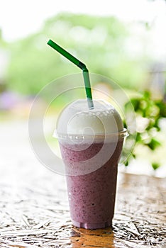 Blueberry smoothie with milk on plastic glass on the wooden table and nature green background - blueberry juice