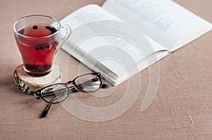Blueberry tea in a clear glass cup on a round wooden stand with glasses