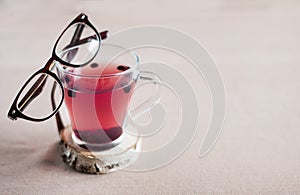 Blueberry tea in a glass cup and with glasses in a brown frame on it,