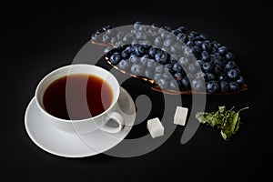 Blueberry on a wooden plate, cup with tea, sugar and dry leaves of mellisa
