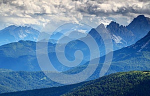 Bluish mist and dark clouds over forested ridges Dolomiti Italy