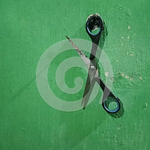 a blunt pair of scissors hanging on a green wall