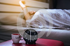Blur asian woman wake up stretch oneself and yawn on the bedroom with black alarm clock 6 o`clock