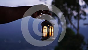Blur background of hand holding a lantern in the dark. Person carry light of lantern in the night