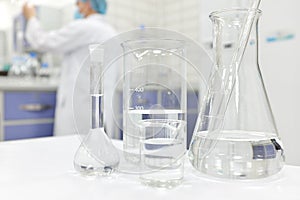 Blur male scientist working in a Chemistry Science laboratory with flask, beaker and glassware containing clear liquid chemical.