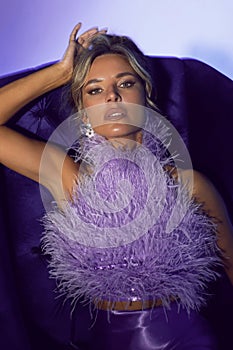 blur portrait of a sexy woman in a purple dress with feathers sitting on a chair in a studio on a cycloram.