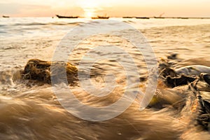 Blur of of Sea spray with small fishing boat background at shore during sunset