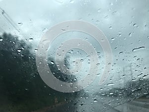 Blur stormy gray sky and rain shot through car`s front windscreen while driving