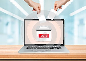 Hand holding and putting voting paper card in ballot box on laptop screen.