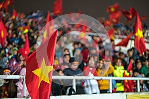 Blurred background of crowd of Vietnamese football fans at My Dinh stadium. Supporter with red clothes raising flags.