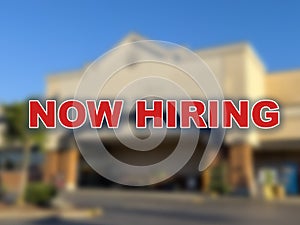 Blurred background of the front of a retail store building with the words Now Hiring in the foreground