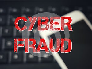 Blurred background keyboard and smartphone with text CYBER FRAUD.