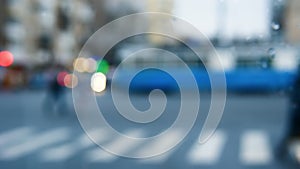 Blurred background of a pedestrian crossing on a motorway. Glowing traffic lights are blurry, people are crossing the road