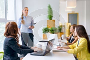 Blurred background. Pretty young business woman giving a presentation in conference or meeting setting. People and