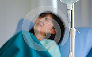 A blurred background of a young ill woman who is lying and coughing on hospital bed, has a saline solution set to intravenous drip