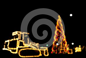 Blurred/bokeh Christmas tree and bulldozer/tractor decorated with lights .