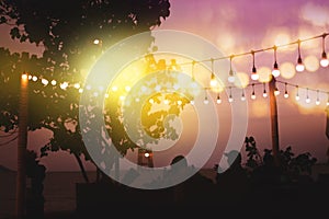 Blurred bokeh light on sunset with yellow string lights decor in beach restaurant