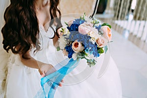 Blurred Bride holds bouquet with creamy roses and peonies and blue hydrangeas. Wedding morning. Close-up