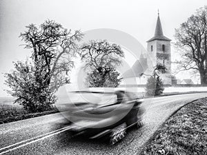 Rozmazaný pohyb auta na silnici se starým kostelem na pozadí
