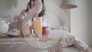 Blurred caucasian woman taking fresh apple from table and crawling away on bed at home. Happy smiling lady eating