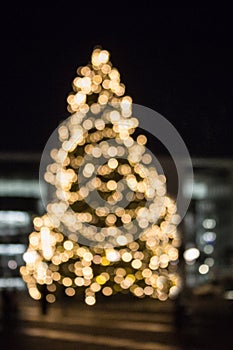 Blurred Christmas tree silhouette illuminated and decorated with golden lights
