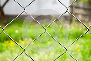 Blurred countryside view through a metal fence on green grass and a house