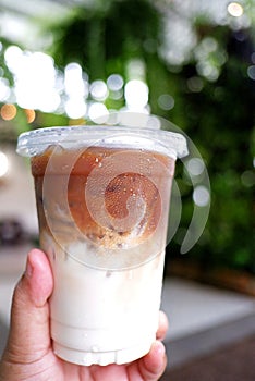 Blurred a cup of iced latte coffee on female hand with green nature background and bokeh light